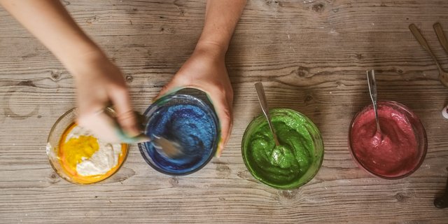 Hands mixing vibrant natural food colorings in bowls on a wooden table.