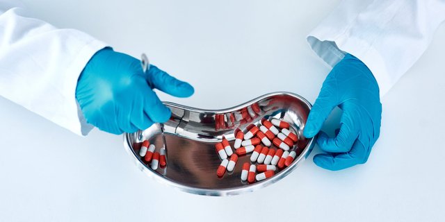 A pharmaceutical researcher wearing blue gloves sorting red-and-white capsules on a stainless steel tray