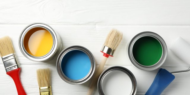 A couple of paint cans on a white table with three brushes and a paint roller.