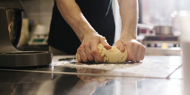 Seorang baker sedang menguleni adonan di meja dapur,