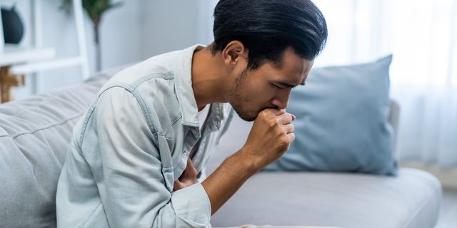 A man experiencing difficulty breathing, holding his chest while sitting in discomfort.